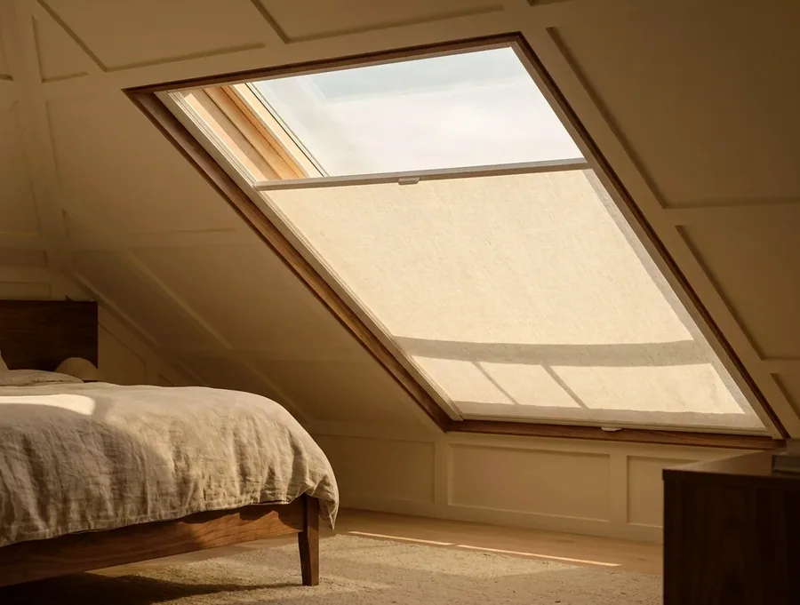 Blind fitted into a sloped skylight above a bedroom, softening the overhead light